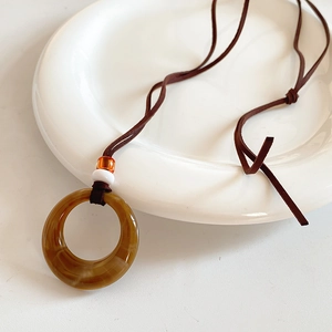 Close-up of resin round pendant necklace with amber ring on white ceramic plate