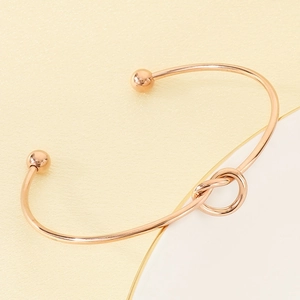 Detail of rose gold knotted open bangle with sphere ends on textured surface