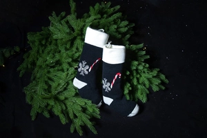 Close-up of black knitted Christmas socks with snowflake and candy cane patterns on pine branches