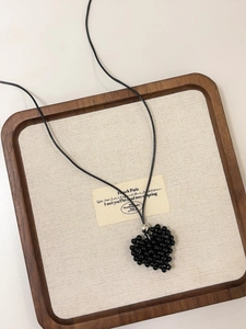 Detail of a black beaded heart pendant on a minimalist necklace against a cream canvas