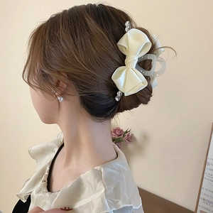Detail of a cream satin bow hair claw clip with rhinestones worn by a model