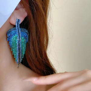 Close-up of model wearing blue rhinestone leaf tassel earrings with sparkling silver finish