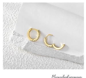 Macro detail of gold-plated hoop earrings with micro-inlaid zirconium on textured stone