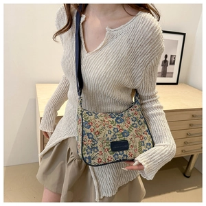 Detail of floral tapestry handbag showing colorful embroidery and dark leather logo patch