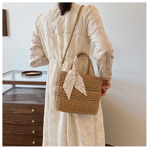 Detail of hand-woven straw crossbody bag with floral scarf and leather shoulder strap
