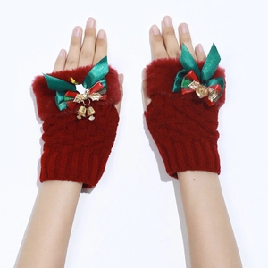 Detail of red Christmas knit fingerless gloves with fur trim and green bow bell