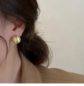 Close-up of a matte gold circular stud earring with brushed metal texture on female model