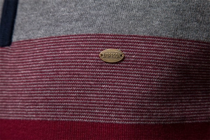 Détail de la maille et de la plaque logo en métal sur un pull rayé pour homme