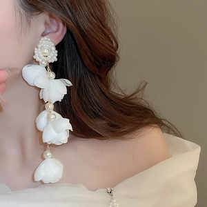 Close-up of long tassel earrings featuring delicate fabric flowers and white pearls