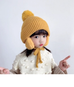 Close-up of ginger yellow kids knit earflap hat with fluffy faux fur pom-pom detail