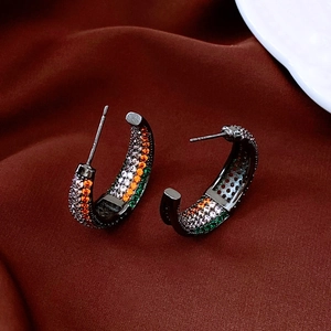 Macro view of C-shaped gunmetal earrings featuring orange, white, and green pave-set zircons