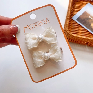 Detail of cream fabric bow hair clips with faux pearls on handmade display card