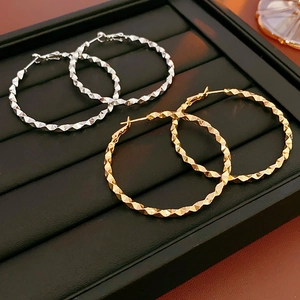 Close-up of gold and silver irregular hoop earrings with faceted texture on black tray