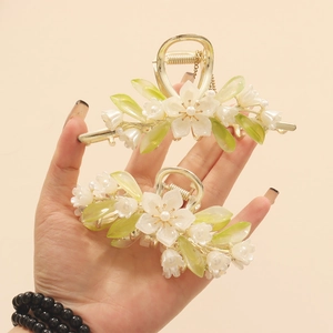 Detail view of two gold flower claw clips with white petals and green leaf accents