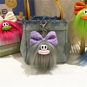 Dettaglio di portachiavi mostro in peluche grigio con fiocco su borsa di jeans