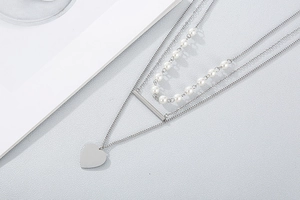Detail of layered stainless steel necklace with pearl chain, bar and heart pendant