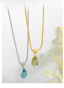 Detailed view of teardrop crystal pendants in blue and olive green with gold snake chains