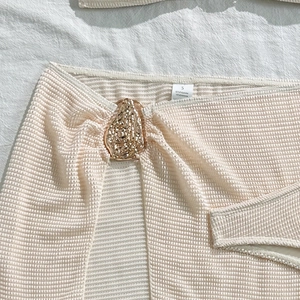 Detail of knit beach skirt with gold buckle, waffle texture and fabric composition tag