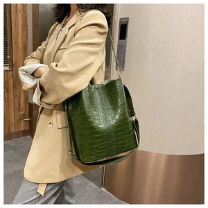Detail of green crocodile-patterned bucket bag with wide strap on shoulder of a model