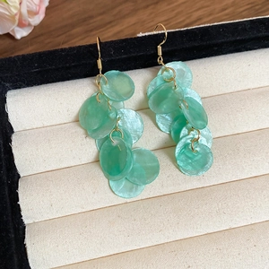 Detailed view of long shell drop earrings with pale green discs on a jewelry display stand