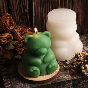 Detailed view of a green bear candle next to its translucent silicone mold on a wooden base