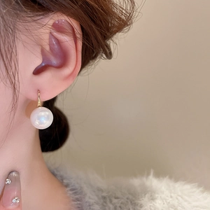 Close-up of a white round pearl earring with golden hook worn by a model