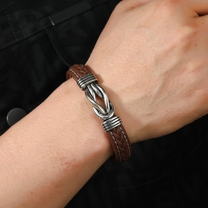 Detailed close-up of brown braided leather bracelet with silver knot magnetic clasp on wrist