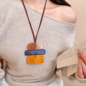 Detail of colorful geometric acrylic pendant on long cord necklace with a beige sweater
