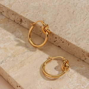 Detailed close-up of golden knotted hoop earrings on a textured stone surface