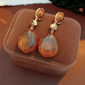 Detail of amber resin teardrop earrings on brown velvet, featuring vintage gold accents