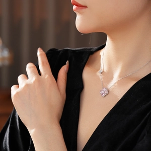 Macro detail of a silver necklace with a pink zircon clover pendant on a model neck
