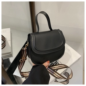 Detail of black saddle bag featuring a stylish wide striped shoulder strap and smooth PU leather