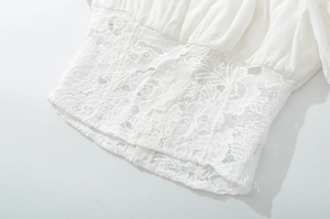 Detail of white cotton top featuring intricate lace embroidery and floral cutout textures