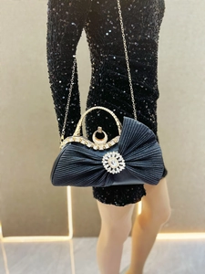 Close-up of luxury pleated black evening clutch with crystal buckle and gold handle