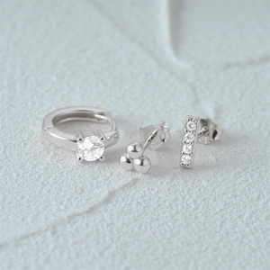 Macro shot of a three-piece silver earring set featuring sparkling zircon studs and hoops