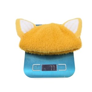 Ginger yellow knitted cat ear hat for children weighing 77g on a blue scale