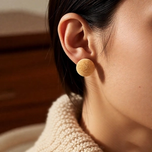 Detail of yellow flocked spherical stud earrings worn with a cozy autumn knit sweater