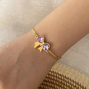 Detailed close-up of a golden bow bracelet with purple heart crystals on a model wrist