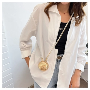 Detail of golden shell-shaped mini crossbody bag with elegant white pearl strap handle