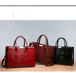 Close-up of crocodile pattern tote bags in red, brown, and black with metal hardware details