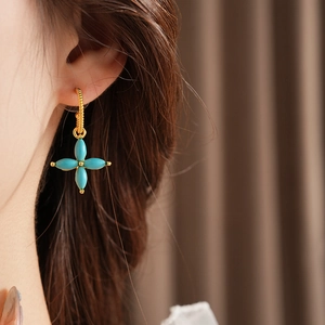 Close-up of a gold clover earring with green stones worn by a model in soft lighting
