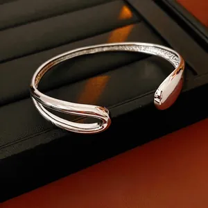 Silver plated open water drop bangle featuring a minimalist asymmetric hollow design