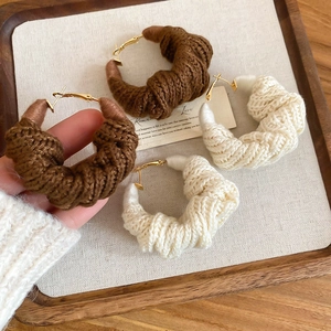 Dettaglio di orecchini a cerchio invernali con trama a spirale in lana marrone e crema