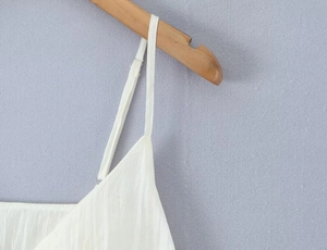 Detailed view of white ruffled camisole top with crinkled texture on wooden hanger
