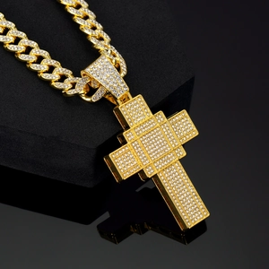 Close-up of golden iced-out cross pendant and Cuban chain on black geometric display