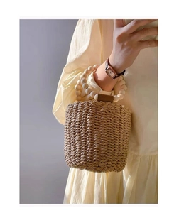 Detailed close-up of handmade straw bucket bag with dark brown leather and wooden bead handle