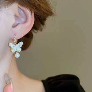 Dettaglio di orecchini a farfalla dorati con smalto, zircone e perle su una modella