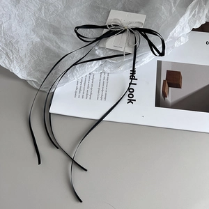 Detail of a black ribbon bow hair clip with silver beaded tassels on a display card