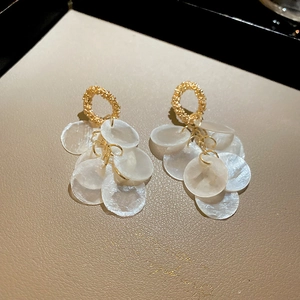 Detailed top view of gold round earrings with white shell pendants on beige leather background
