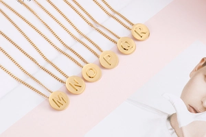 Detail of round gold pendant necklaces featuring engraved letters M to R on a magazine backdrop